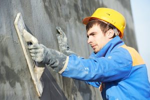 Young builder worker at facade plastering work during industrial